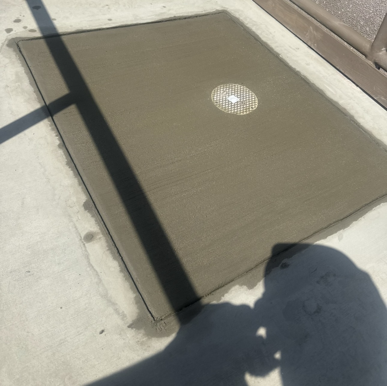 Freshly poured concrete patch with a round brass sewer cleanout cover set flush in the surface