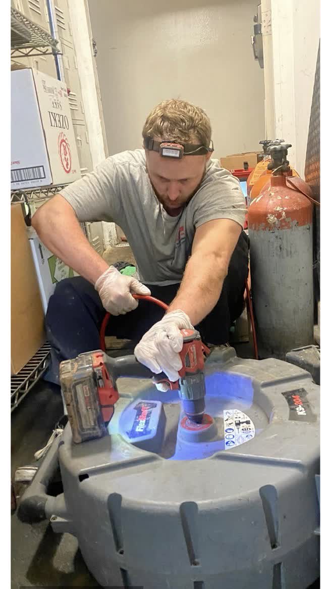 Plumbing technician wearing gloves and a headlamp using a power tool while servicing equipment