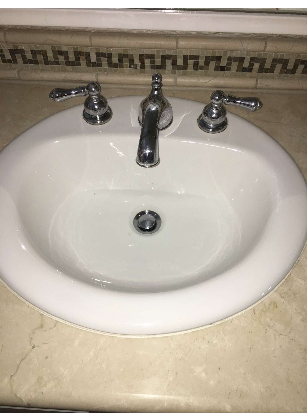Chrome widespread faucet with two lever handles on a white oval drop-in bathroom sink set in a marble countertop