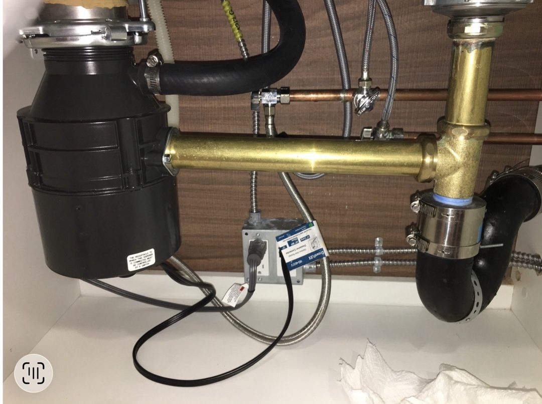 Kitchen sink garbage disposal and connected drain plumbing beneath the cabinet
