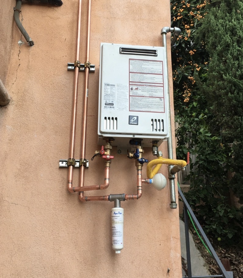 Exterior wall-mounted tankless water heater with copper piping, gas line, and inline water filter