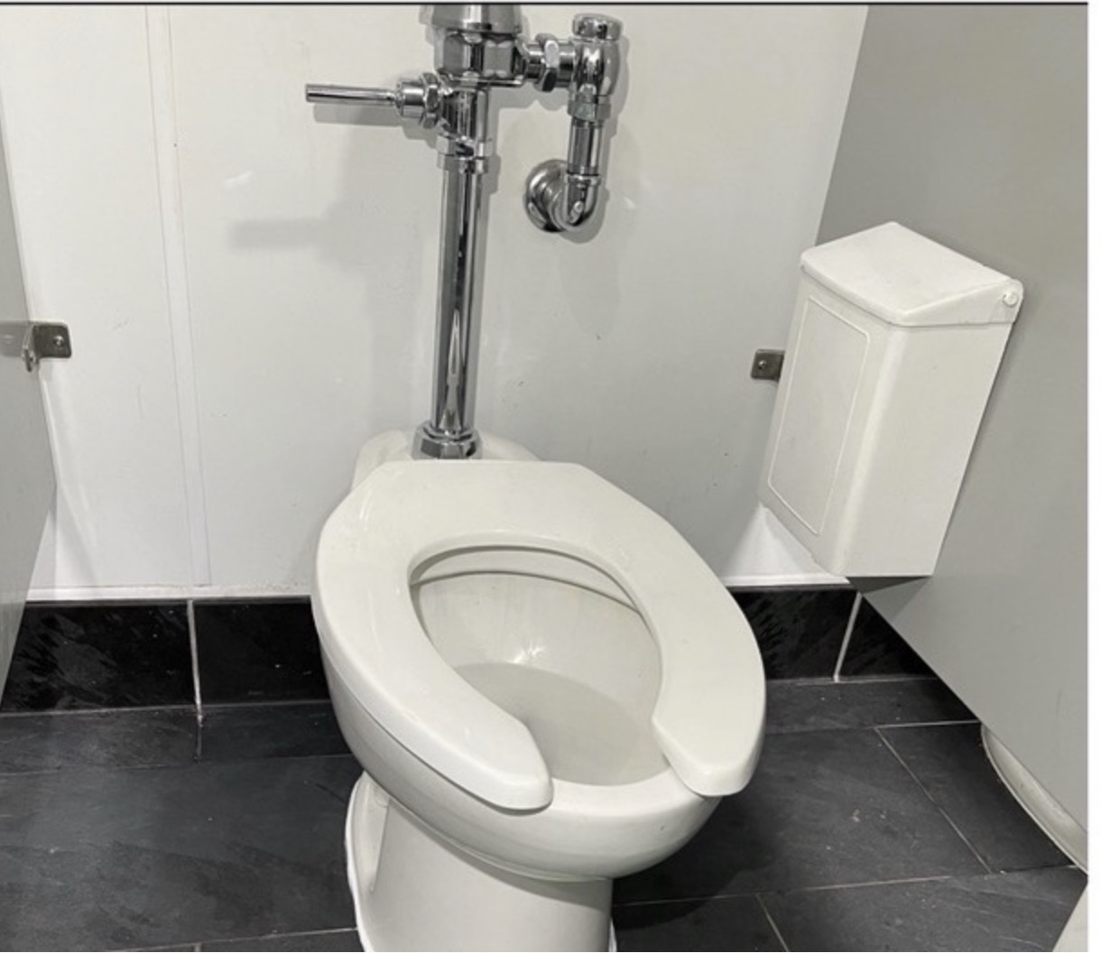 Commercial restroom toilet with a chrome flush valve installed against a white partition
