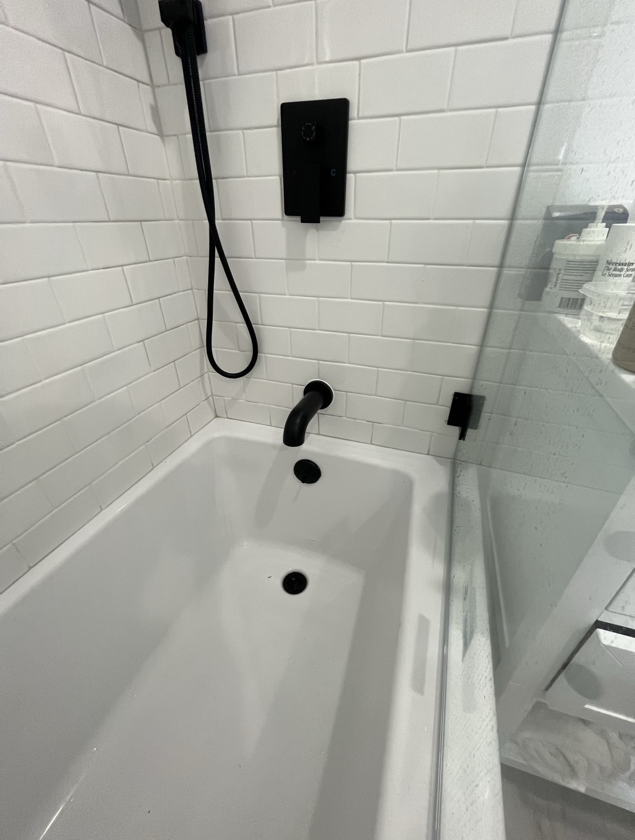 White bathtub with matte black tub spout, handheld sprayer, and wall valve on white subway tile
