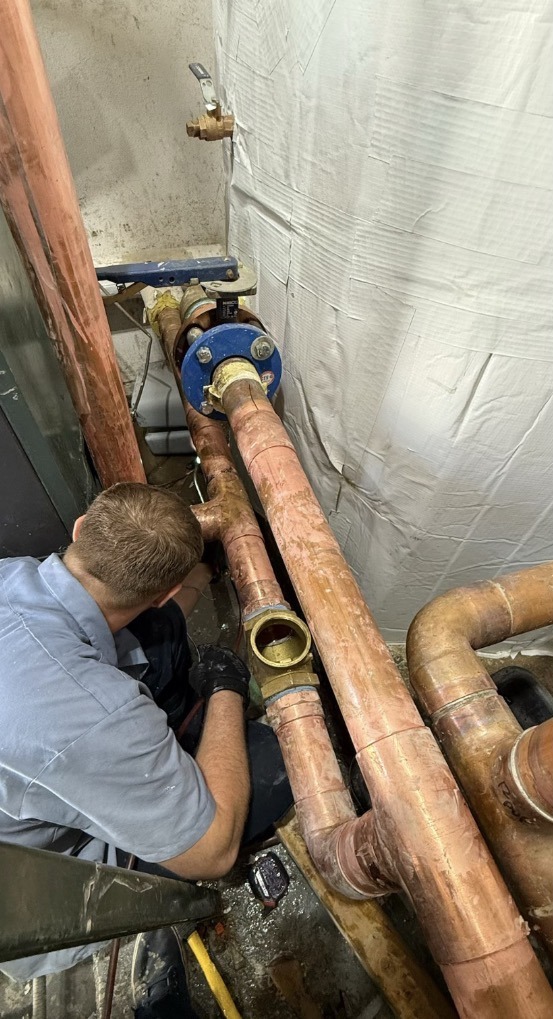 Plumbing technician performing hands-on work on large copper piping
