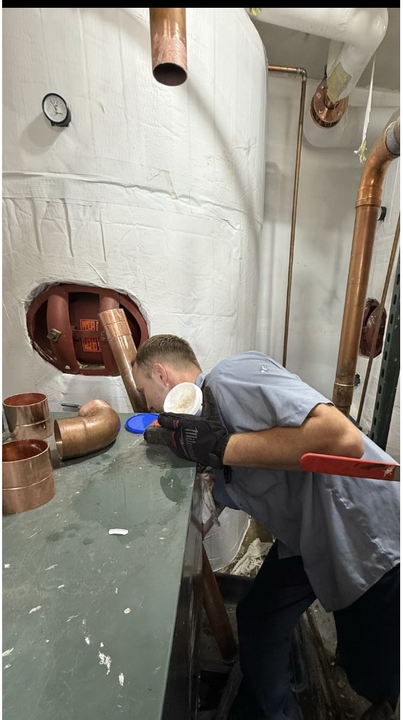 Plumbing technician performing detailed work on a large copper piping system