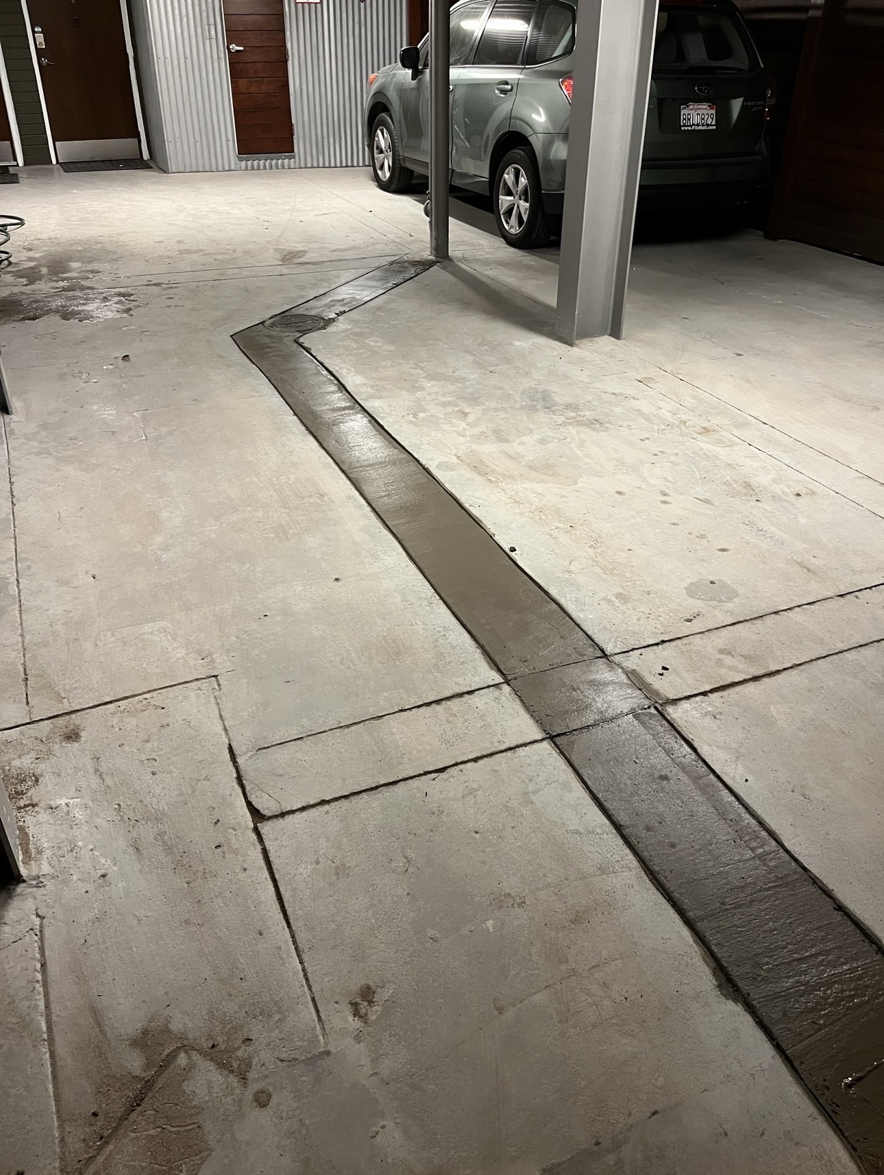 Freshly patched concrete trench line running across a parking garage floor
