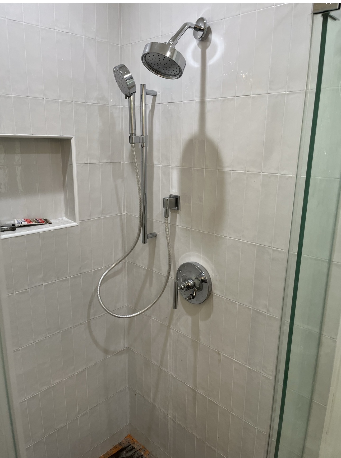 Tiled shower with chrome showerhead, sliding bar handheld sprayer, and single-handle valve trim