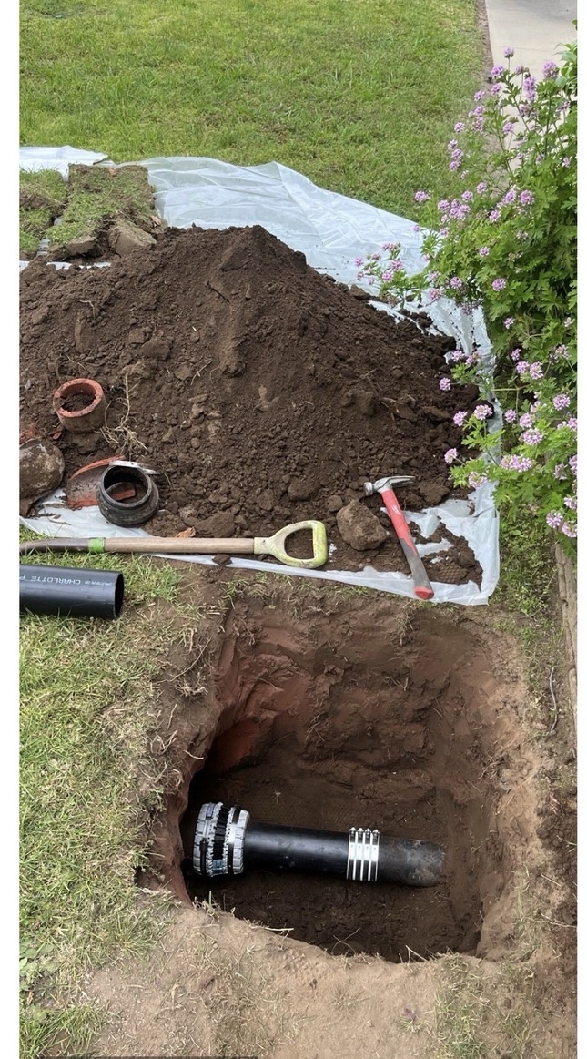 Excavated yard trench exposing a repaired black sewer line with soil piled on a protective tarp