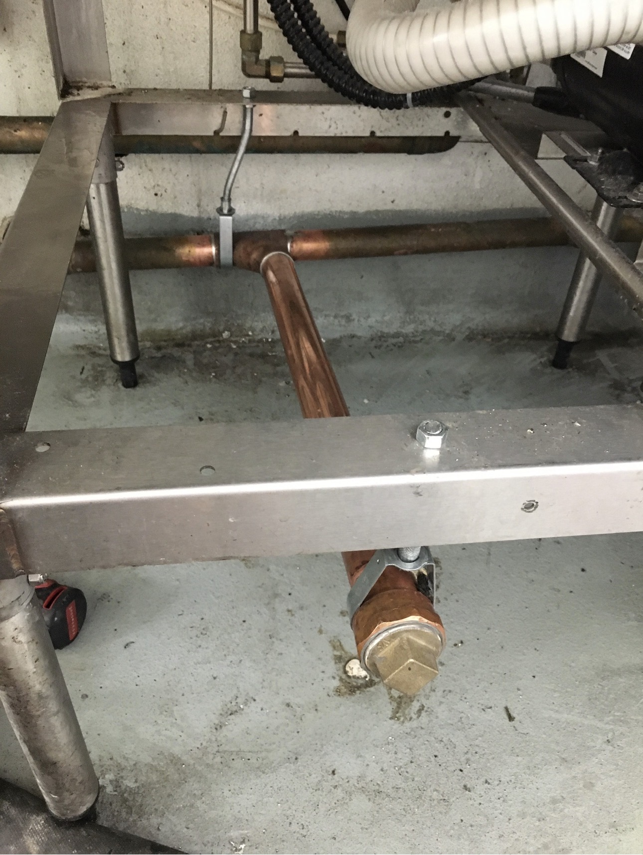 Copper water lines and drain connections routed and strapped beneath a stainless steel commercial kitchen sink frame