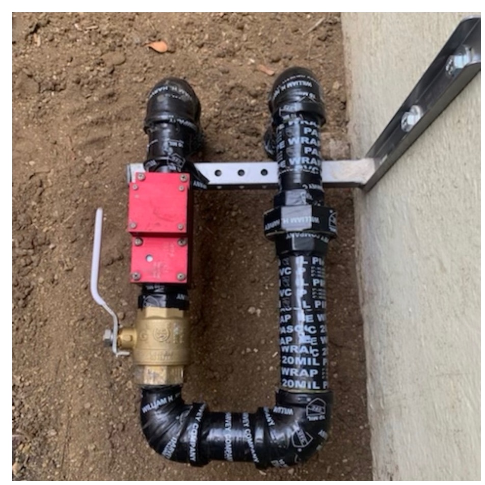 Red earthquake safety valve on a black wrapped gas line with a brass shutoff valve mounted along a wall